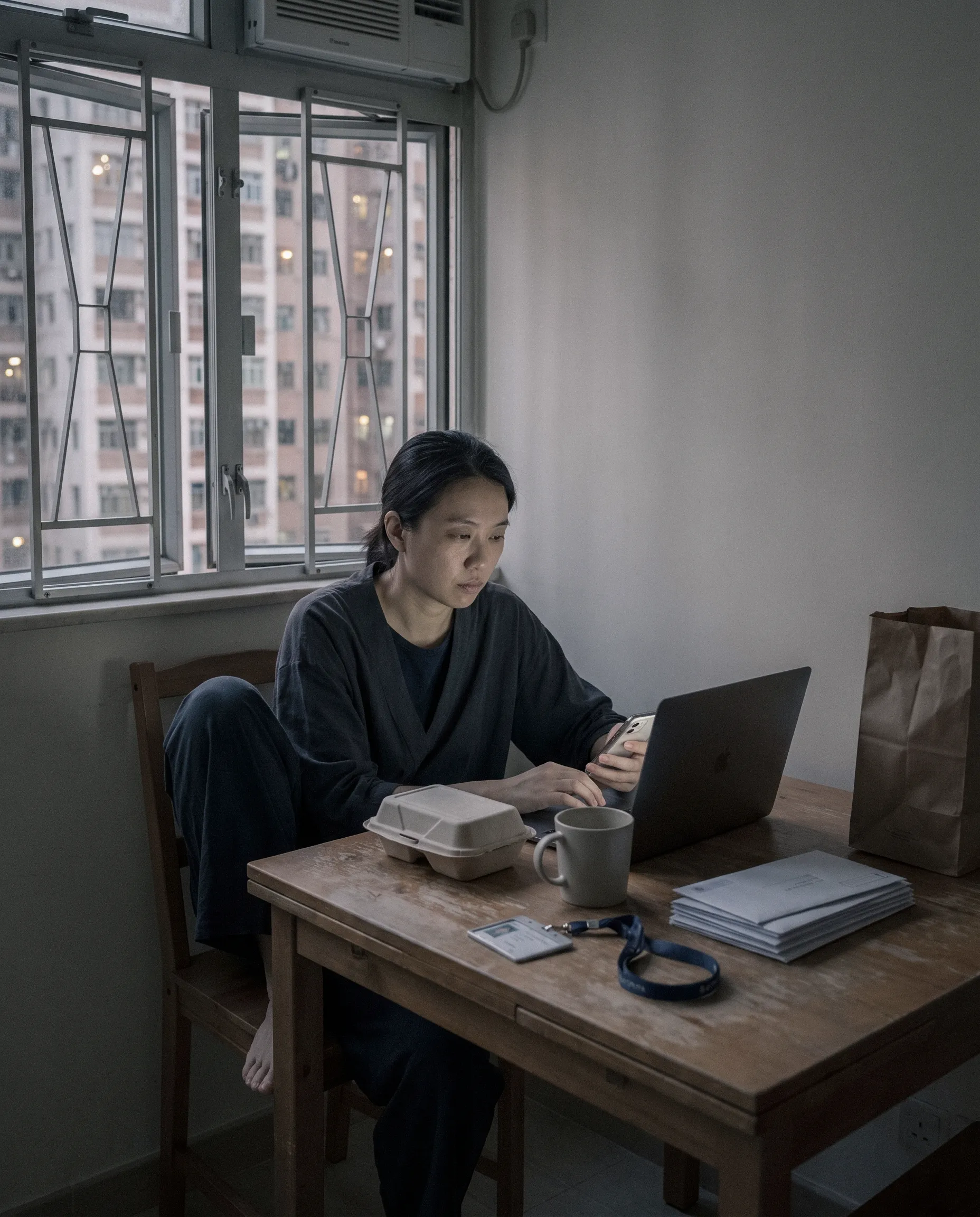 A woman working at a laptop at a dining table in a Hong Kong apartment.